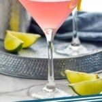 Pinterest graphic for Cosmopolitan Cocktail recipe. Image shows two glasses of Cosmopolitan Cocktail with shaker bottle and lime wedges beside. Text says, "cosmo cocktail simplejoy.com"