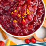 Pinterest graphic for Cranberry Sauce. Image shows a bowl of Cranberry Sauce with orange slices, fresh cranberries and a cinnamon stick sitting beside. Text says "Cranberry Sauce simplejoy.com"