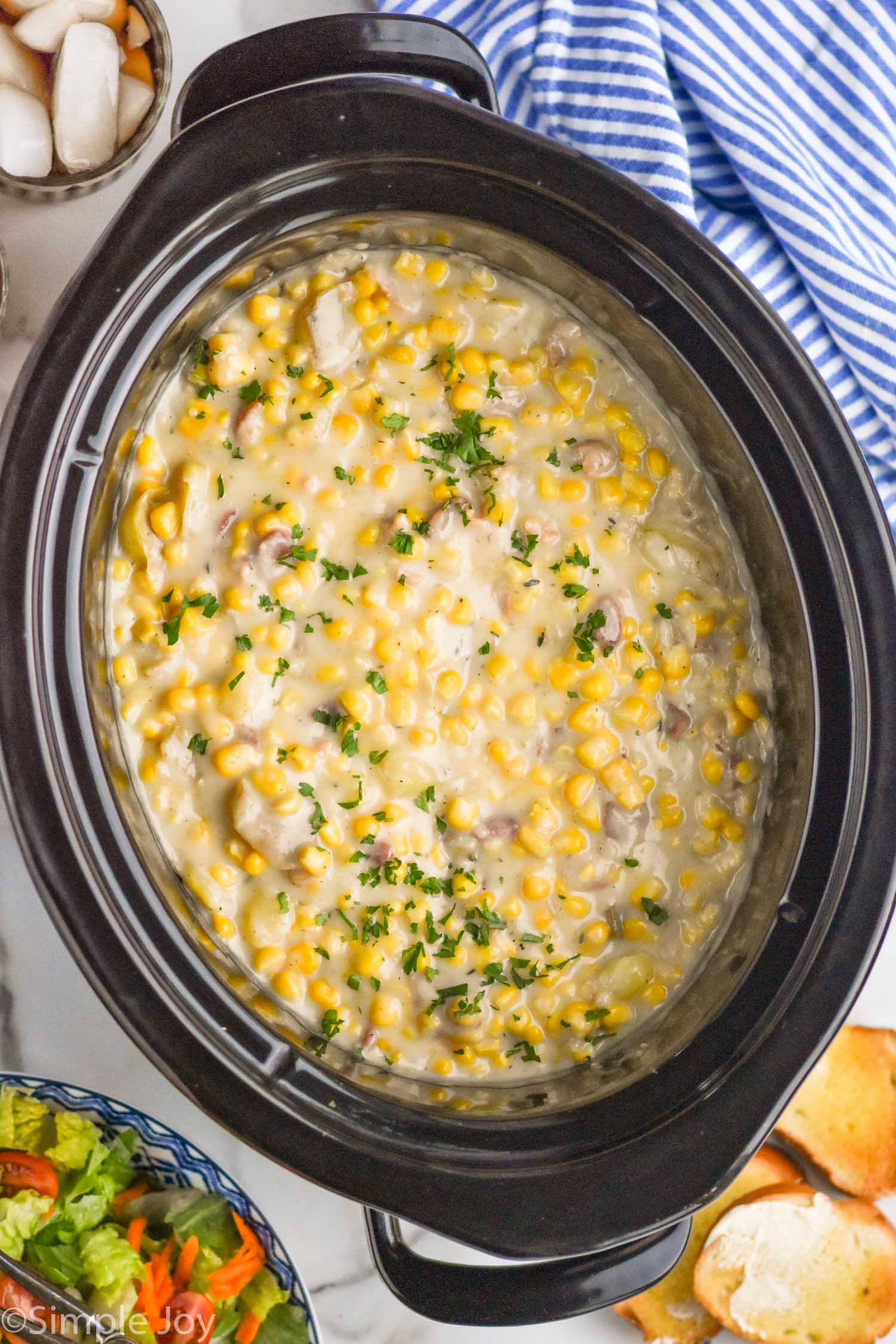 Overhead photo of a crockpot of Crockpot Corn Chowder recipe with salad and bread beside