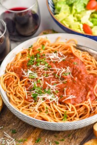 Bowl of pasta with Marinara Sauce. Glasses of wine and bowl of salad beside.