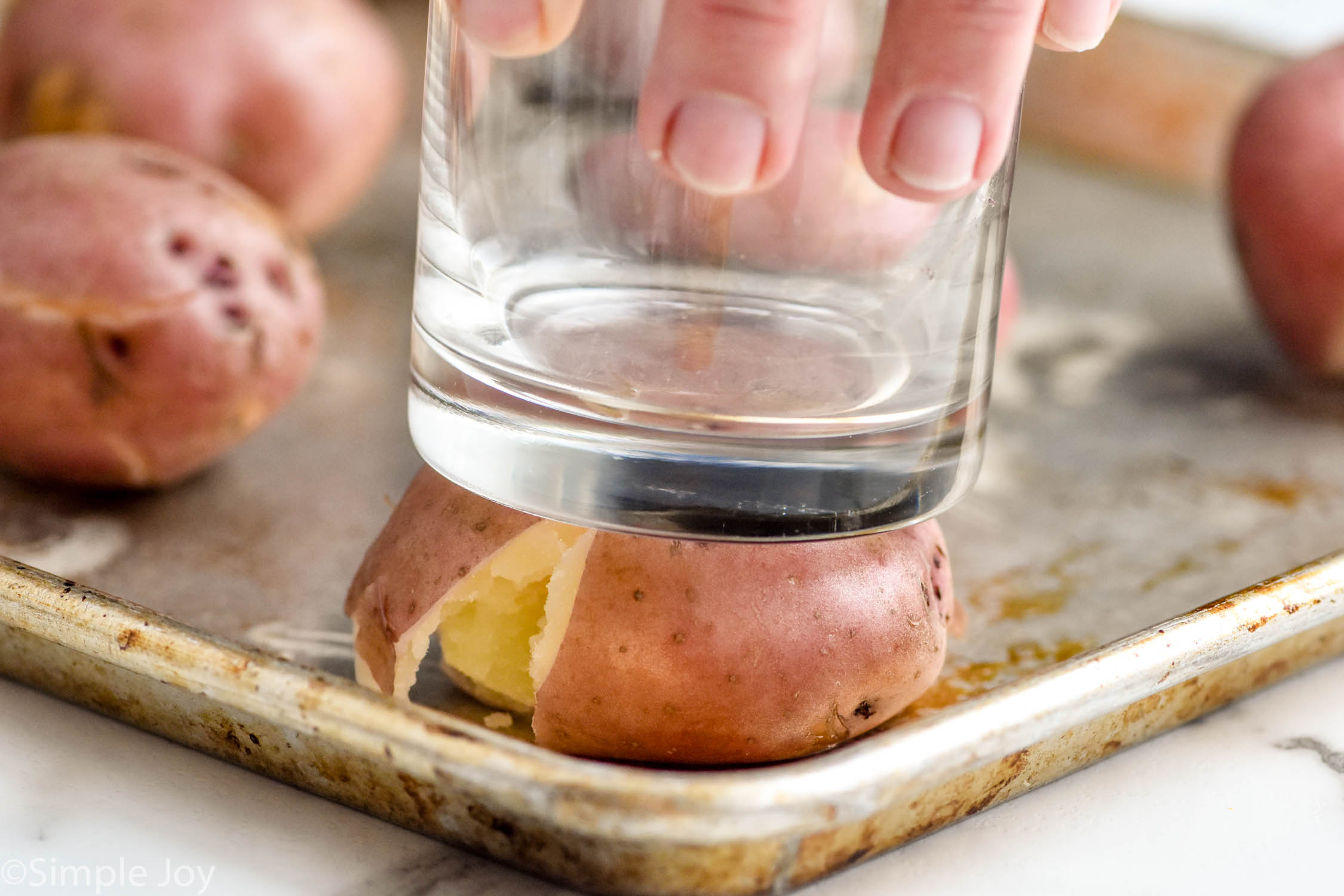 person's hand using glass to smash potato on baking sheet to make Smashed Potatoes