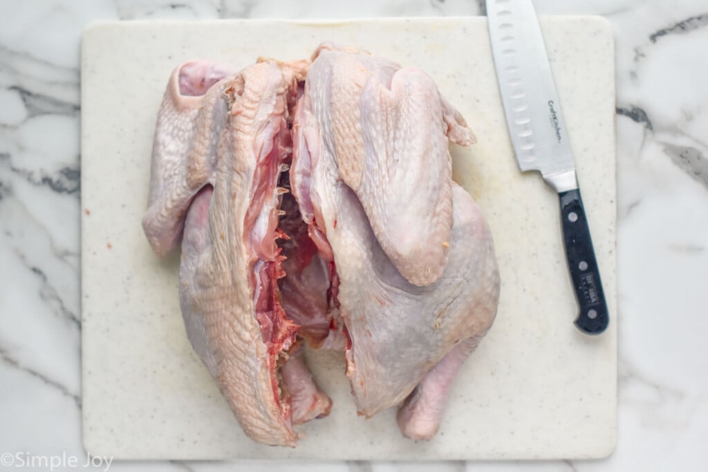 Overhead photo of a raw turkey cut open for Spatchcock Turkey with knife beside