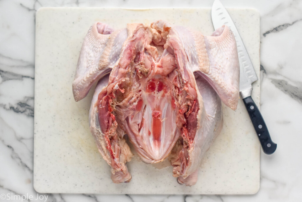 Overhead photo of a raw turkey cut open for Spatchcock Turkey recipe. Knife beside.