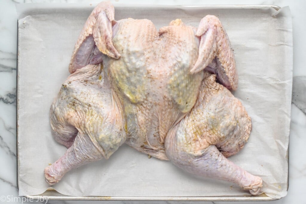 Overhead photo of a raw seasoned turkey on a baking sheet for Spatchcock Turkey recipe.