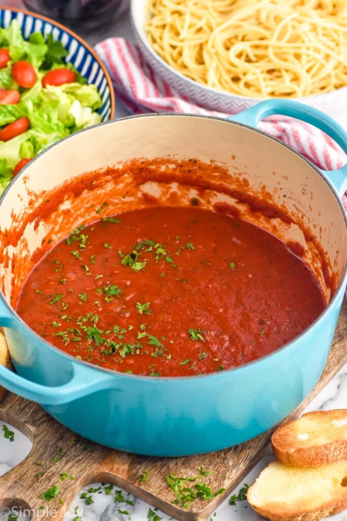 Photo of a pot of Marinara Sauce with bowls of spaghetti and salad beside