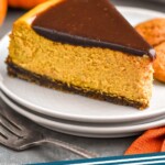 Pinterest graphic for Pumpkin Cheesecake recipe. Image shows a slice of Pumpkin Cheesecake served on a plate. Fork and pumpkin beside. Text says, "Pumpkin Cheesecake simplejoy.com"