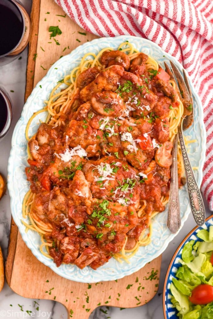 plate of Chicken Cacciatore with a fork for serving. Glasses of red wine and bowl of salad sitting beside.