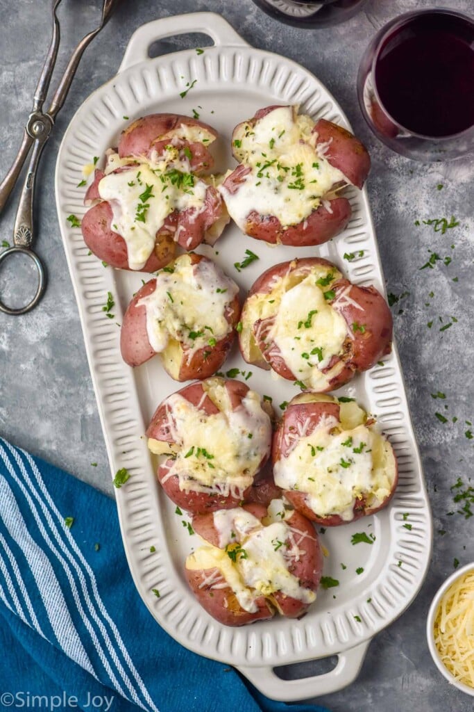 overhead of Smashed Potatoes on a plate with tongs and glass of wine sitting beside