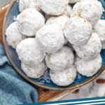 Pinterest graphic for Snowball cookies. Text says "Snowball cookies simplejoy.com" Image shows overhead of a plate of Snowball cookies. Bowl of pecans sitting beside.