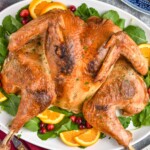 Overhead photo of Spatchcock Turkey on a platter garnished with orange slices, greens, and cranberries. - 12