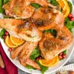 Pinterest graphic for Spatchcock Turkey recipe. Image is overhead photo of a platter of carved Spatchcock Turkey served on a platter of greens, cranberries, and orange slices. Text says, "amazing Spatchcock Turkey simplejoy.com"