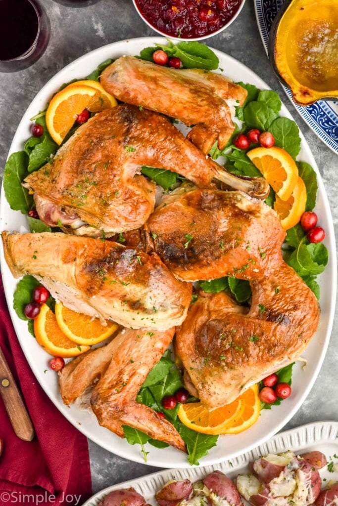 Overhead photo of Spatchcock Turkey carved on a platter of greens, orange slices, and cranberries.