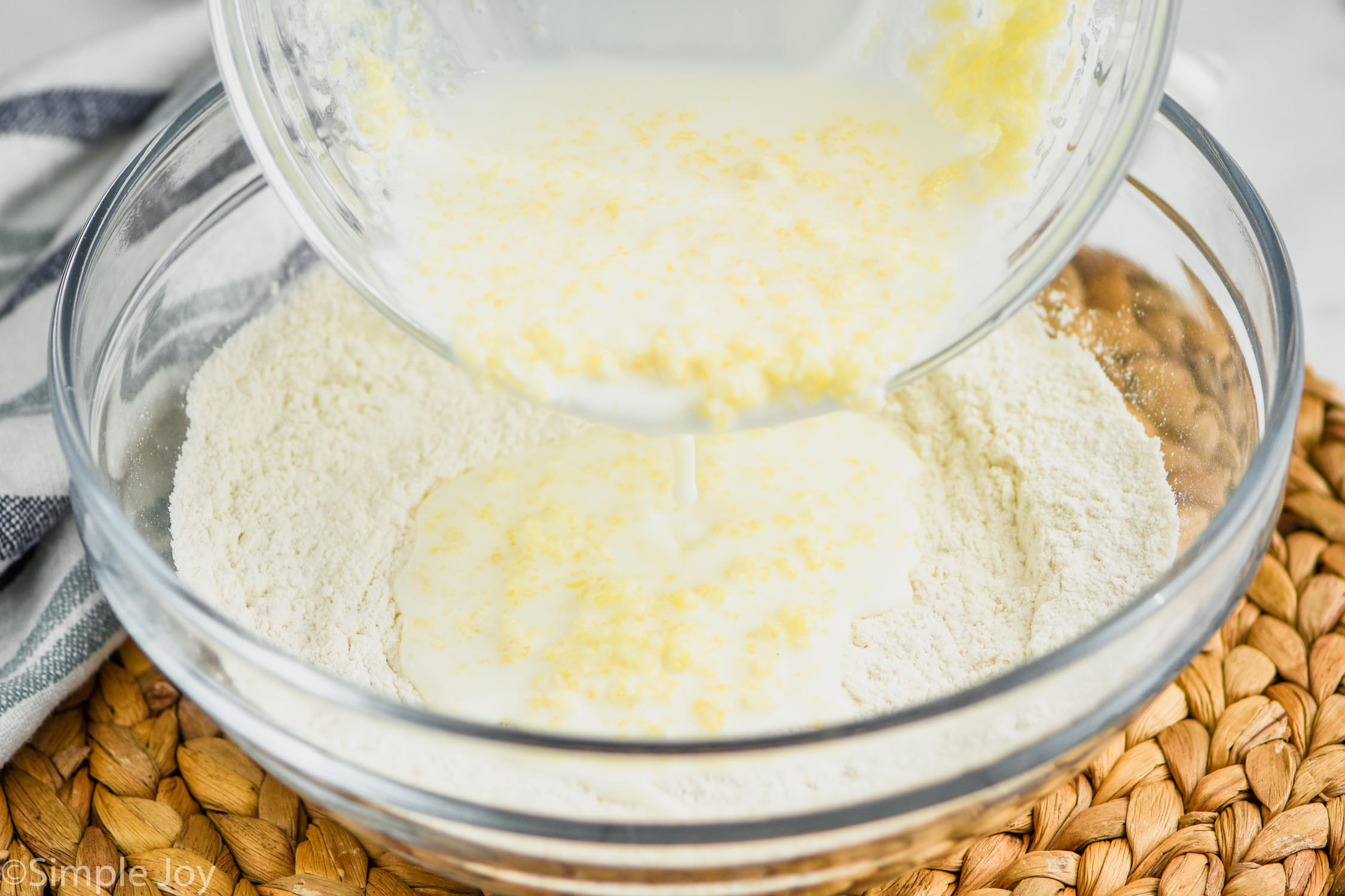 pouring buttermilk mixture from one glass bowl into a flour mixture in another glass bowl to make easy drop biscuits