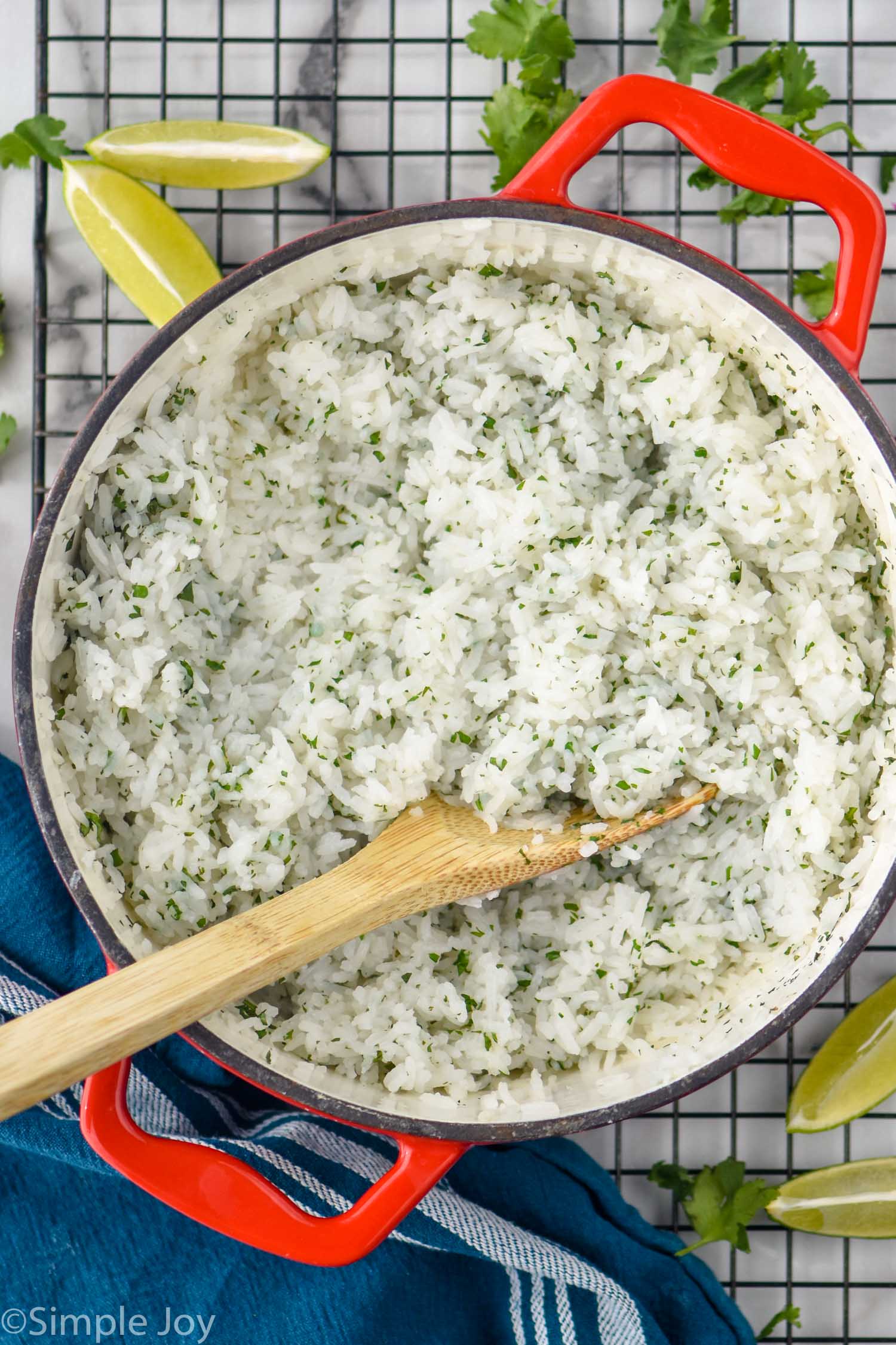 Overhead photo of a pot of Cilantro Lime Rice on a cooling rack with a spoon. Lime wedges and cilantro beside.