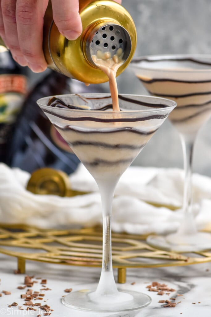 Side view of person's hand pouring cocktail shaker of Chocolate Martini recipe into prepared martini glasses
