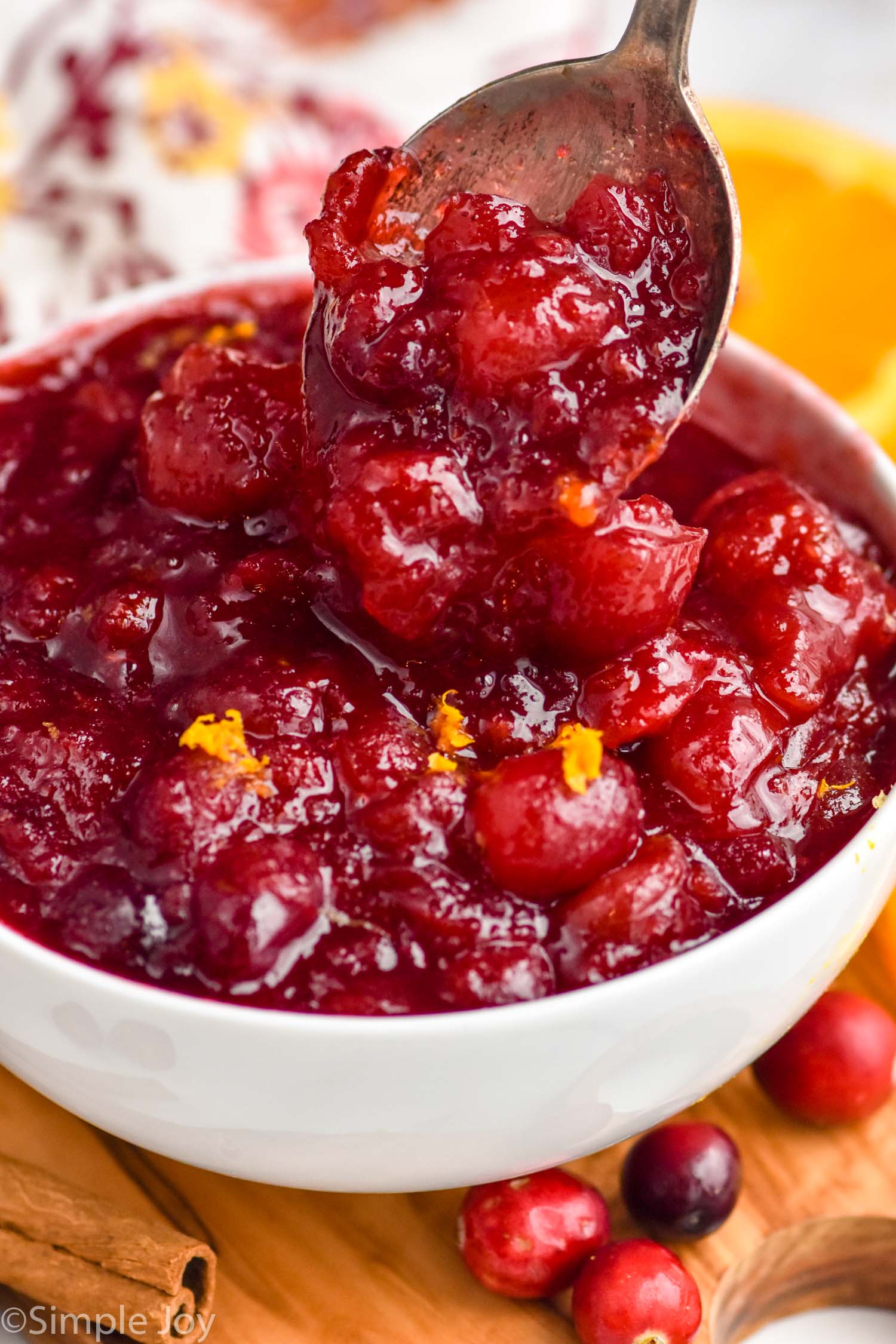 spoon in bowl of Cranberry Sauce. Fresh cranberries, orange slices, and cinnamon sticks surrounding bowl