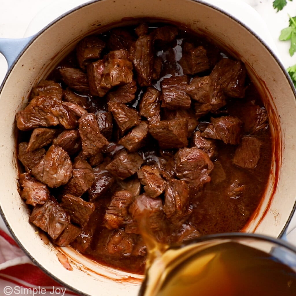 pouring beef broth over seared meat to make beef stew
