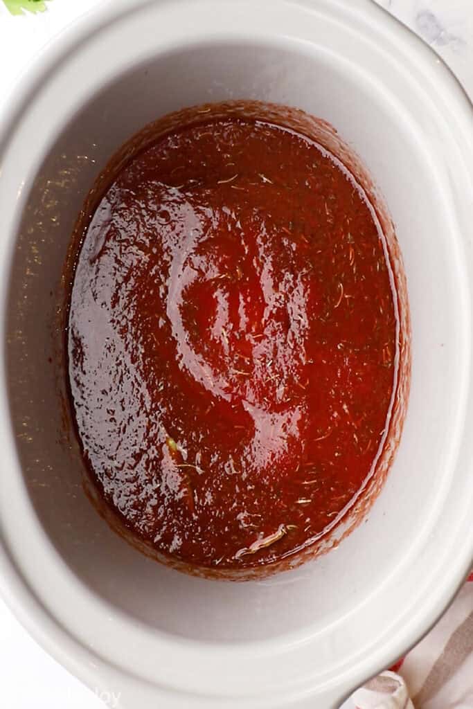 overhead of a red sauce mixed together in the base of a slow cooker