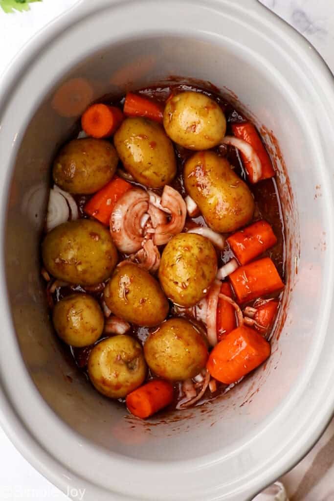 overhead of carrots, potatoes, and onions mixed with sauce in a slow cooker