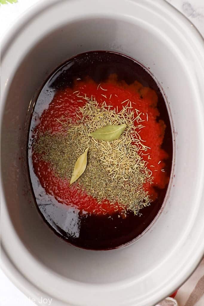overhead of wine, tomato sauce, and spices in a slow cooker