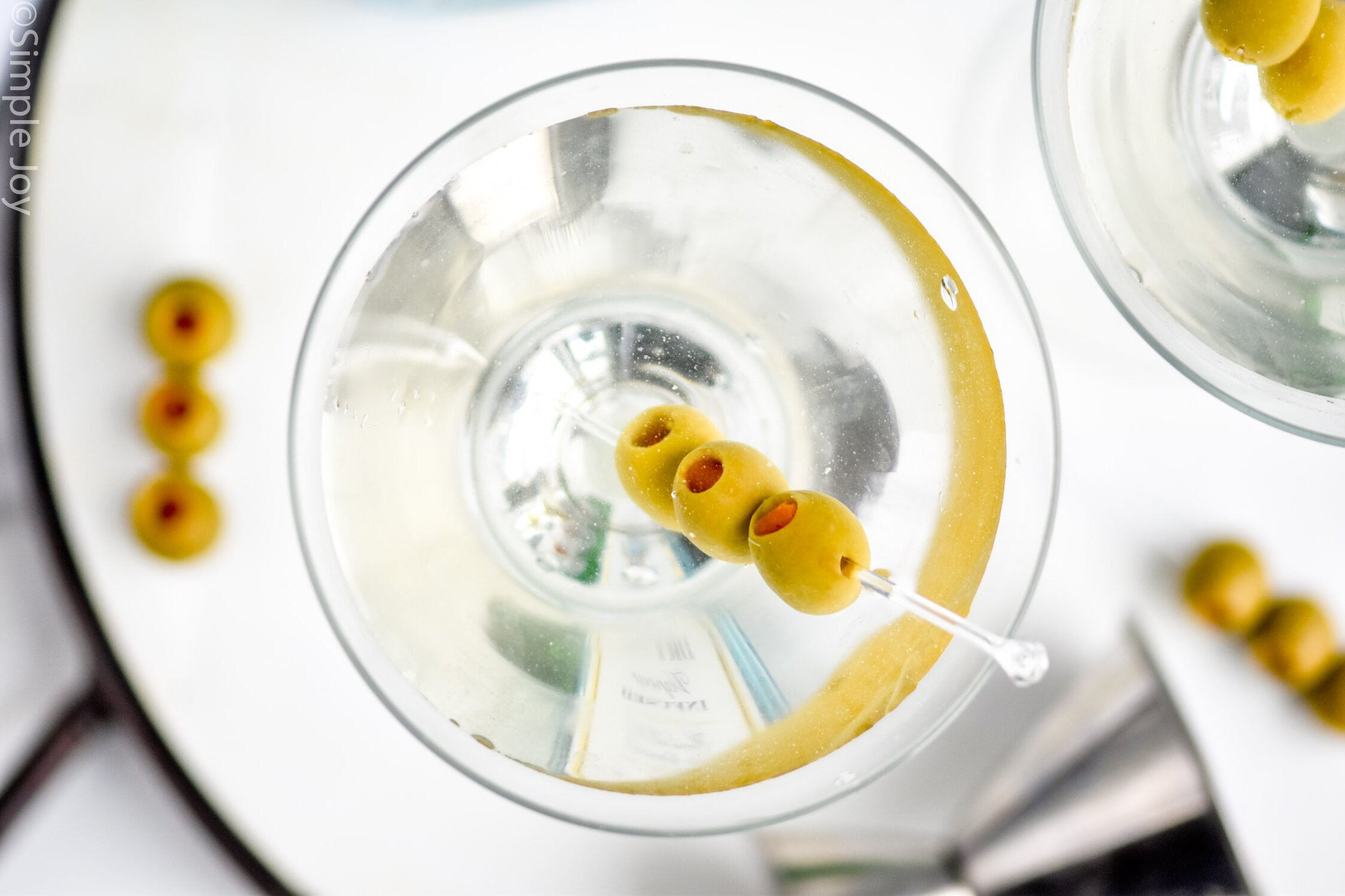 overhead of a gin martini in a glass garnished with three olives on a clear plastic toothpick