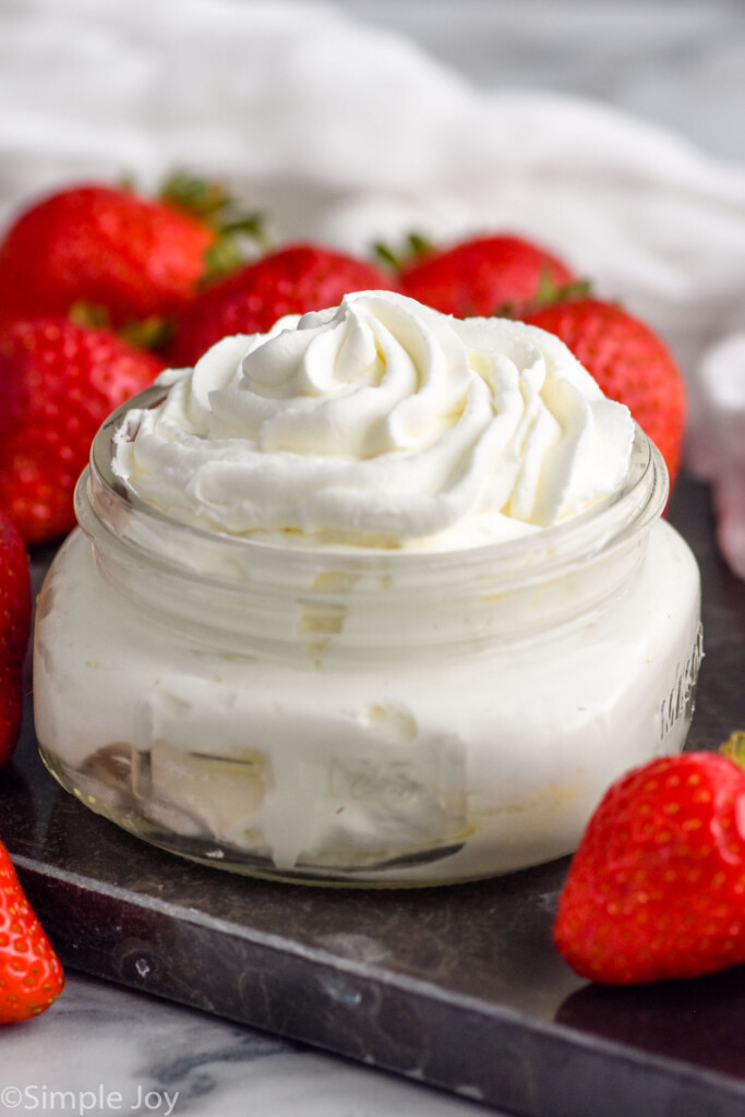 Photo of a jar of Homemade Whipped Cream with strawberries beside