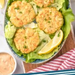 Pinterest graphic for Crab Cakes recipe. Image is overhead view of Crab Cakes on a plate with lettuce and lemon wedges. Dipping sauce and lemon wedges beside plate. Text says, "the best Crab Cakes simplejoy.com"