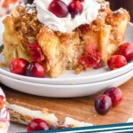 Pinterest graphic for Cranberry French Toast Casserole recipe. Image shows Cranberry French Toast Casserole on a plate garnished with whipped cream and cranberries. Cups of coffee beside. Text says, "Cranberry French Toast Casserole simplejoy.com."