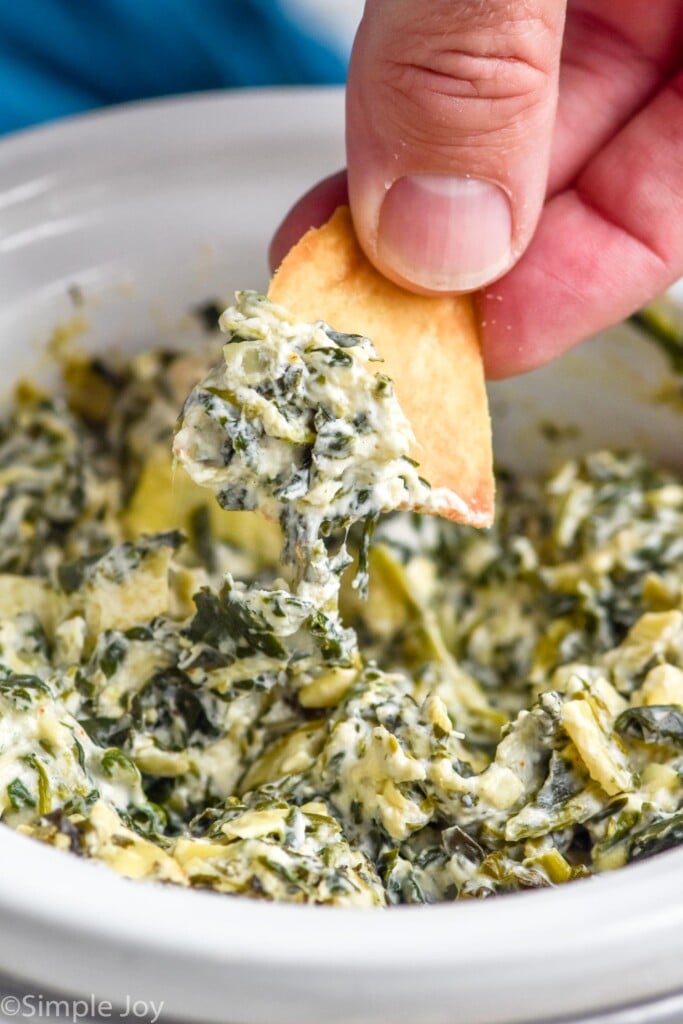 Close up photo of person's hand dipping a chip into Crockpot Spinach Artichoke Dip