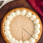 Pinterest graphic for Eggnog Cheesecake recipe. Text says, "the best Eggnog Cheesecake simplejoy.com." Image is overhead photo of Eggnog Cheesecake with one slice cut. Cinnamon sticks and glass of eggnog beside.