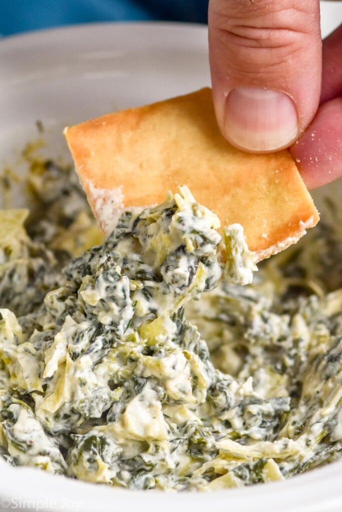 Close up photo of person's hand dipping a chip into Crockpot Spinach Artichoke Dip