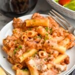 Photo of Baked Ziti served on a plate with a fork. Wine and salad beside.