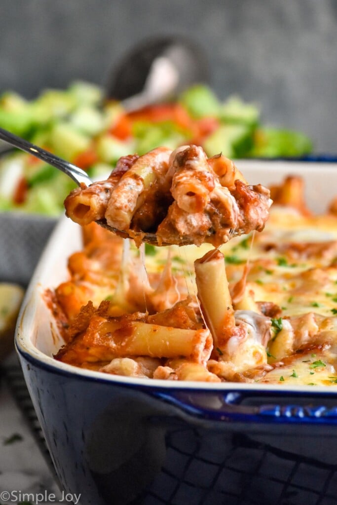 Side view of a spoon scooping out a serving of Baked Ziti from baking dish