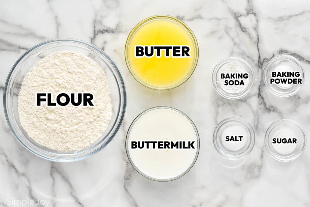 bowls of ingredients for biscuits labeled; flour, melted butter, buttermilk baking soda, baking powder, salt, and sugar