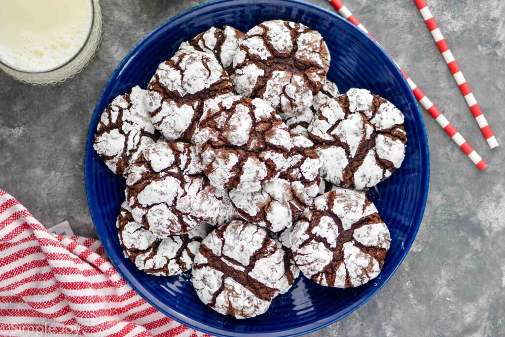 Overhead photo of a plate of Chocolate Crinkle Cookies with a glass of milk beside