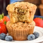 Side view of a stack of two Coffee Cake Muffins with a bite taken out of the top muffin. Berries beside.