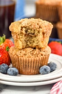 Side view of a stack of two Coffee Cake Muffins with a bite taken out of the top muffin. Berries beside.