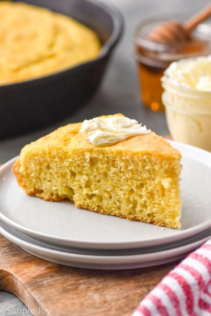 Slice of Skillet Cornbread on a plate with butter. Honey, butter, and Skillet Cornbread beside.