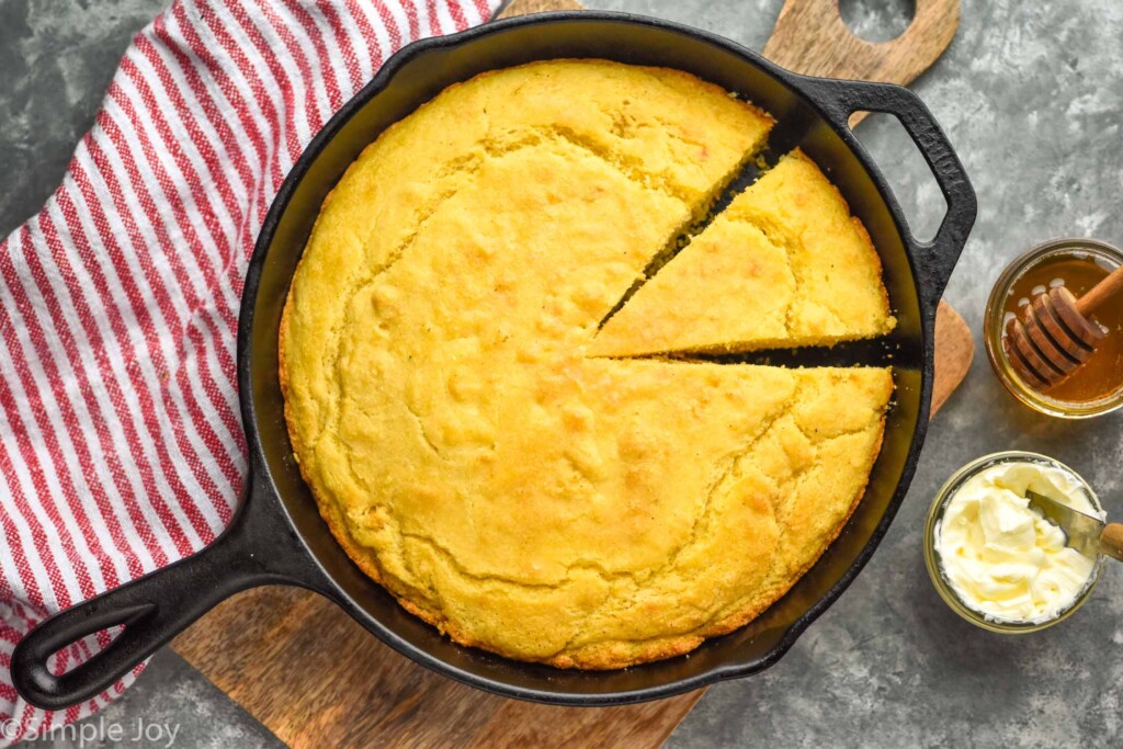 Overhead photo of Skillet Cornbread with a slice cut. Butter and honey beside