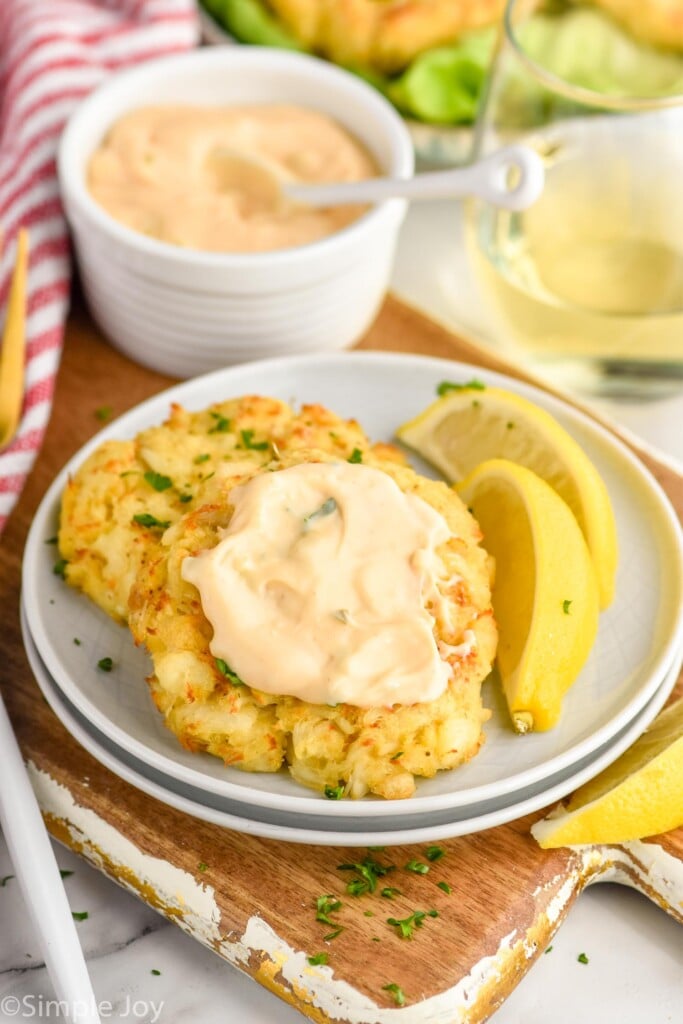 Crab Cakes on a plate with lemon wedges and sauce. Dipping sauce and glass of wine beside.