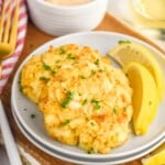 Crab Cakes on a plate with lemon wedges. Sauce and a glass of wine beside. Fork for eating. - 8