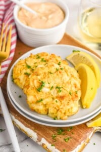 Crab Cakes on a plate with lemon wedges. Sauce and a glass of wine beside. Fork for eating.