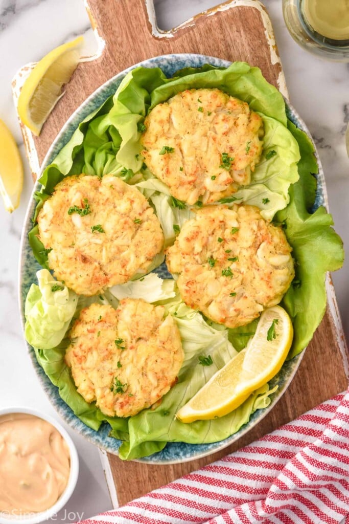 Overhead of Crab Cakes on lettuce with lemon wedges beside. Dipping sauce beside.
