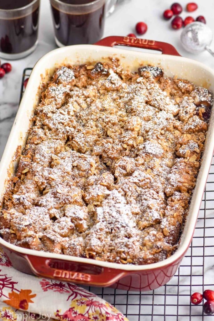 Baking dish of Cranberry French Toast Casserole on a cooling rack. Cranberries and cups of coffee beside