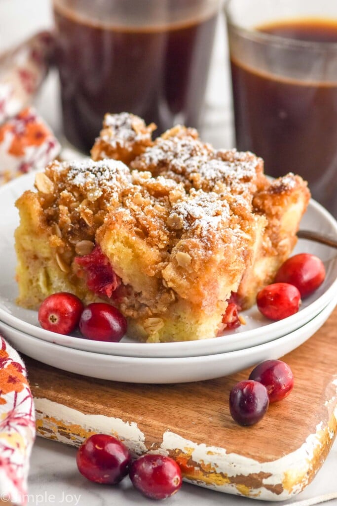 Cranberry French Toast Casserole on a plate with cranberries. Cups of coffee beside.