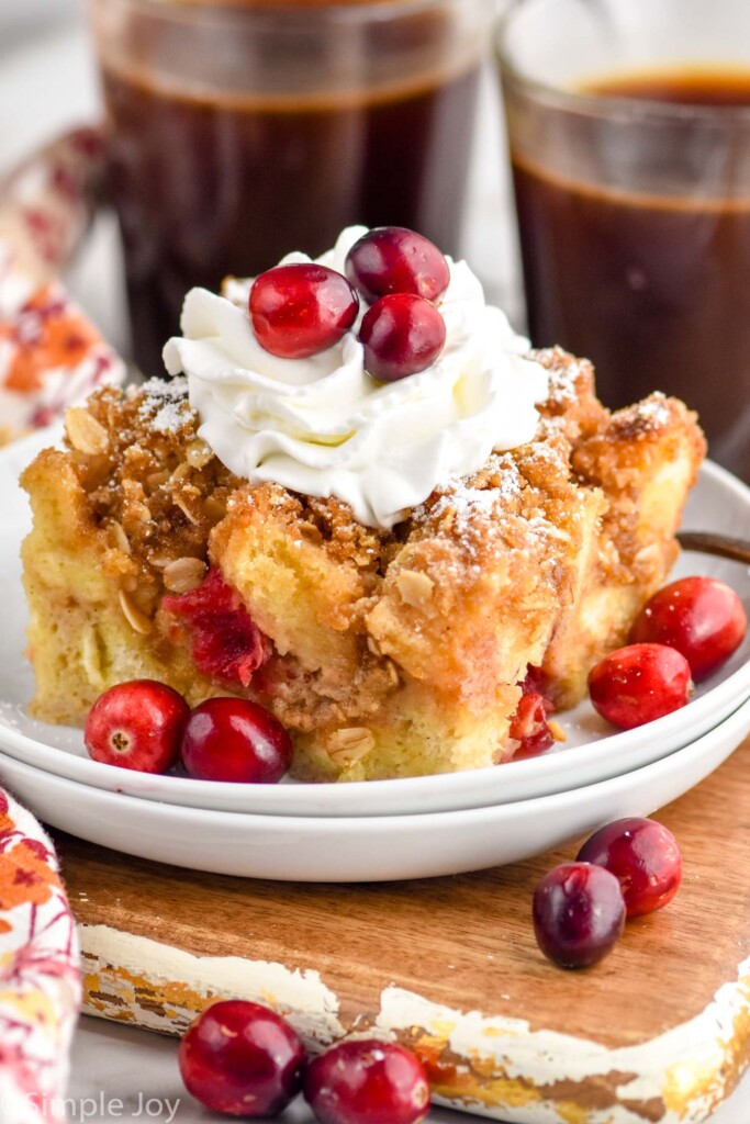Cranberry French Toast Casserole on a plate garnished with whipped cream and cranberries. Cups of coffee beside.