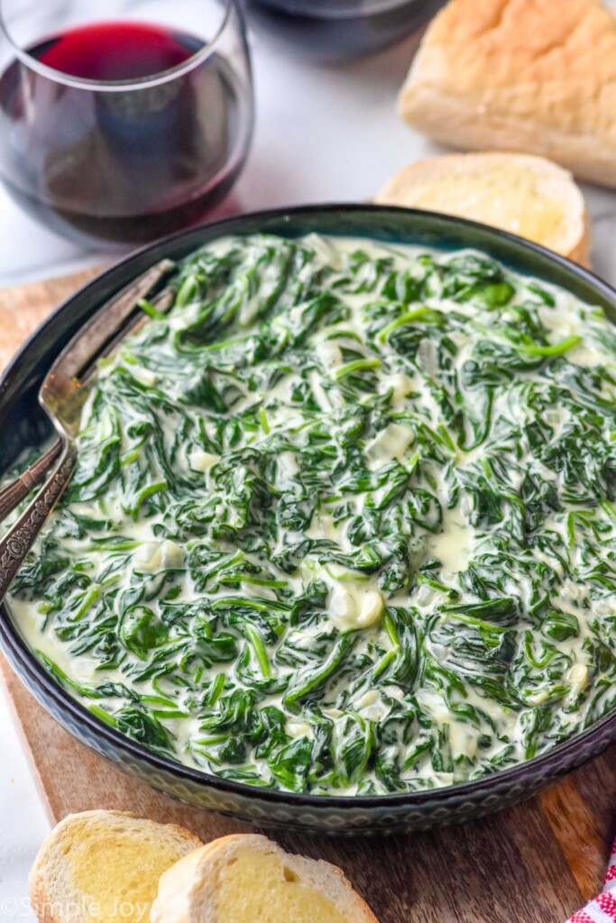 Bowl of Creamed Spinach with bread and glass of red wine beside.