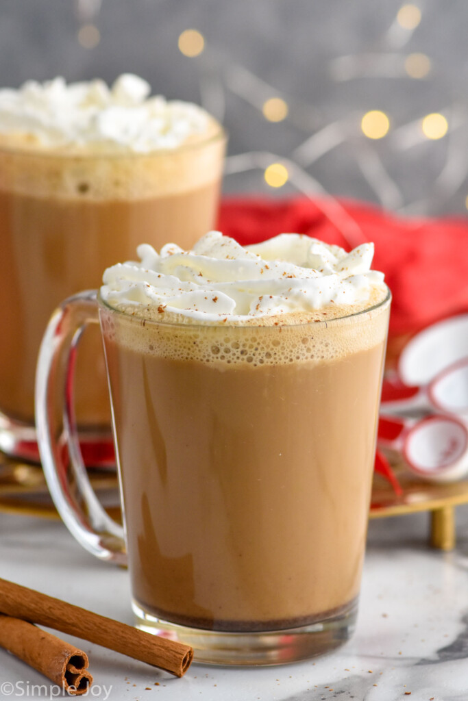 Side view of mugs of Eggnog Latte garnished with whipped cream. Cinnamon sticks beside.