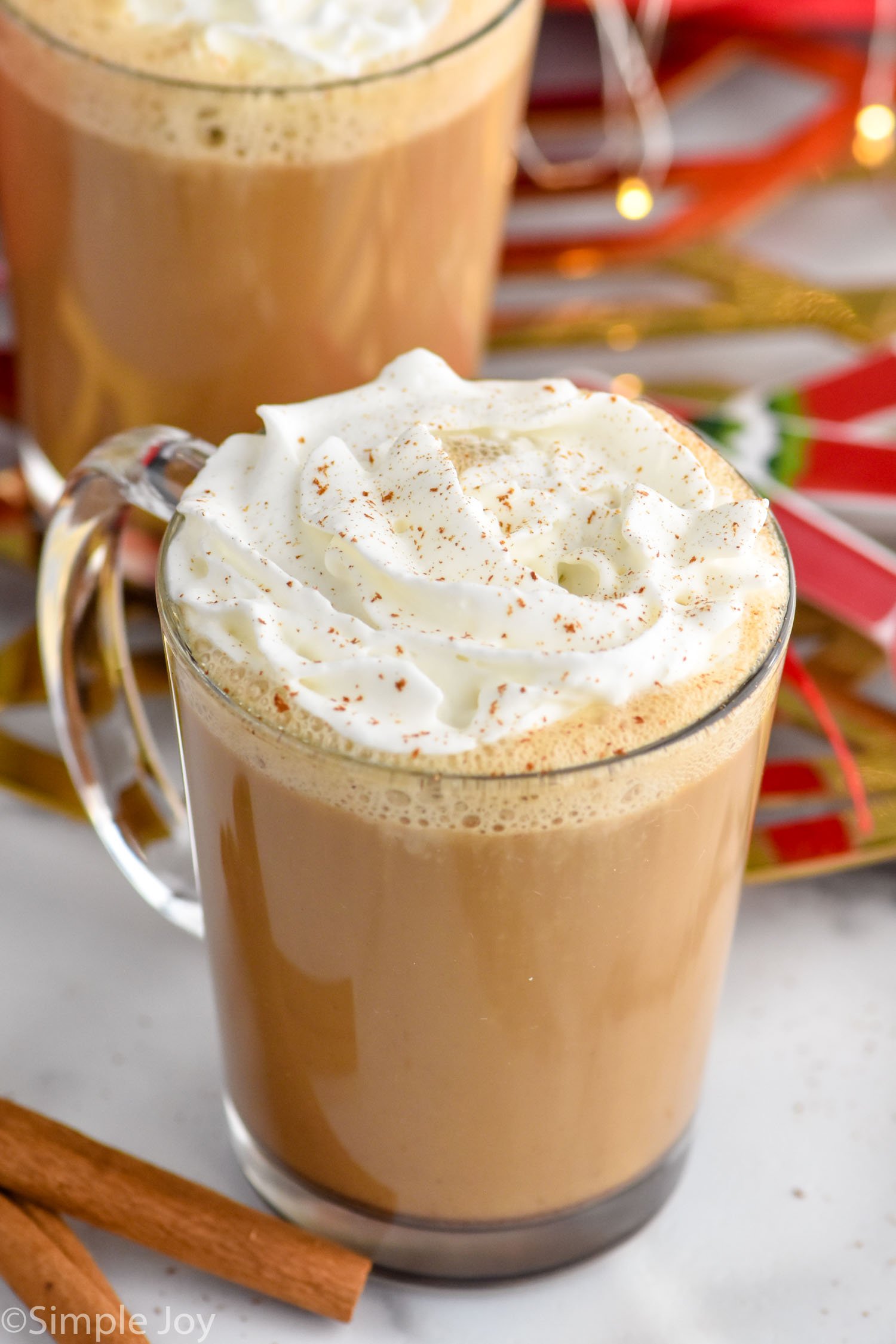 Photo of mugs of Eggnog Latte garnished with whipped cream with cinnamon sticks beside.