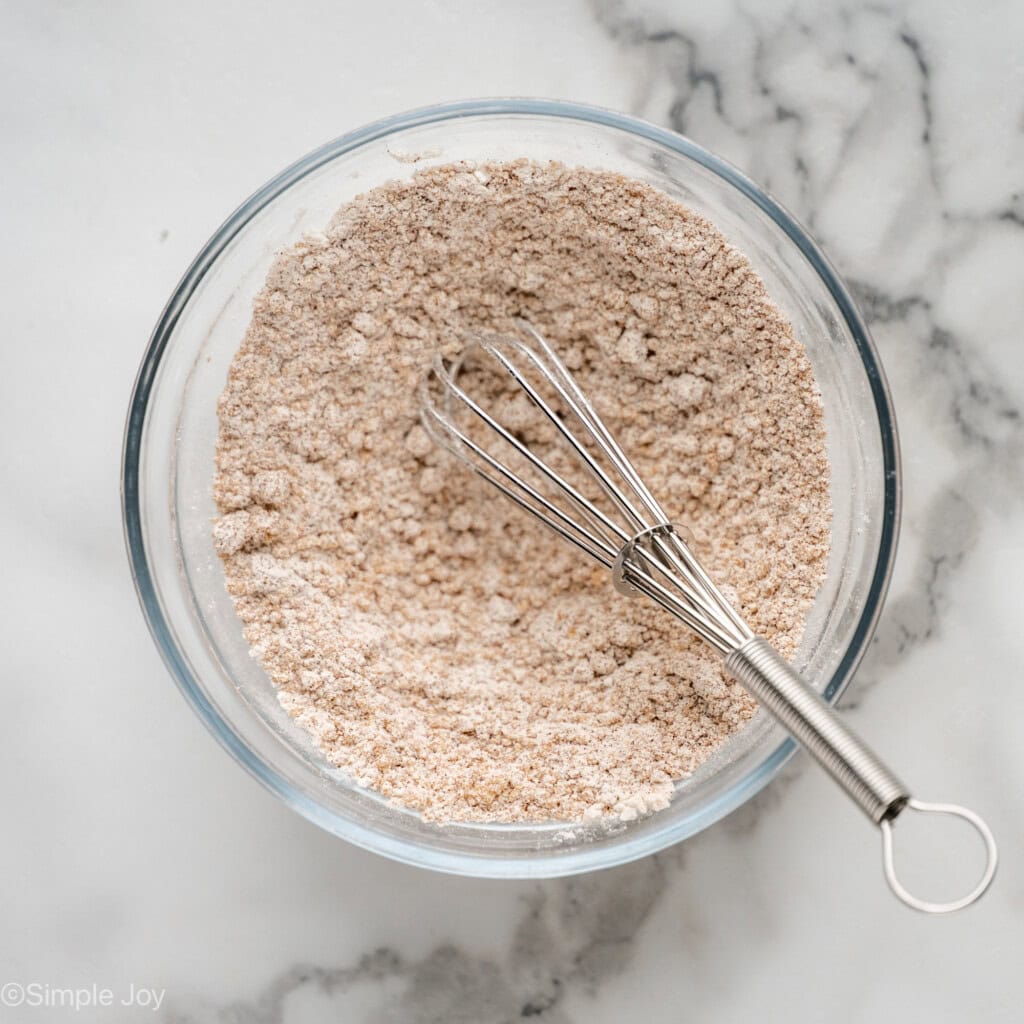 overhead of a bowl of whisked brown sugar, flour, and cinnamon with a small whisk in it